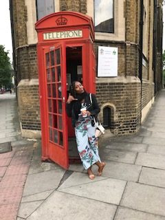 Black woman in London posing in front of the red telephone booth