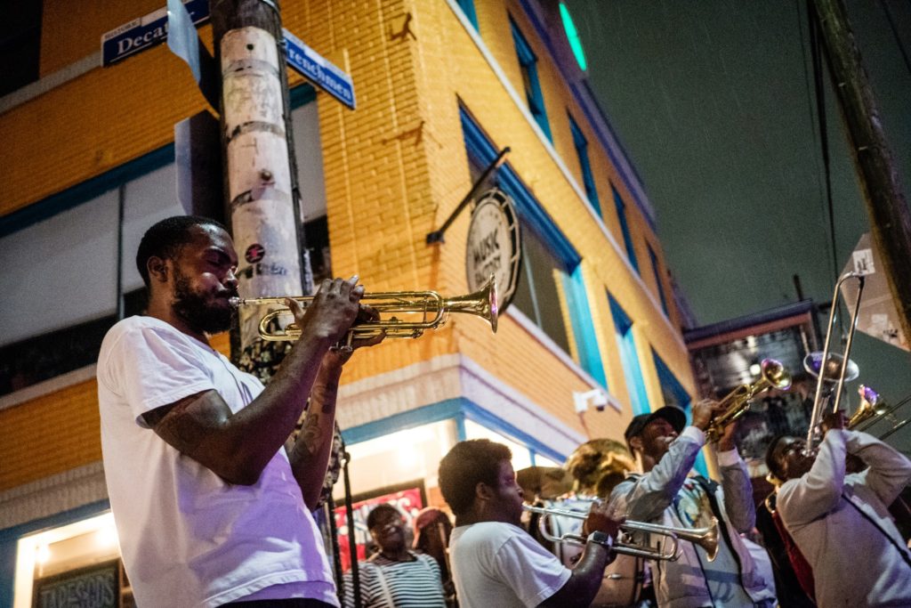 alt txt = "African American men wearing casual clothing playing instruments in the street."