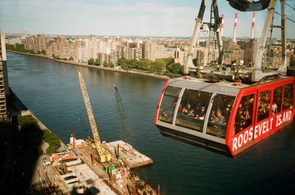 alt txt = "Tram on cable car in the sky above water near a factory."
