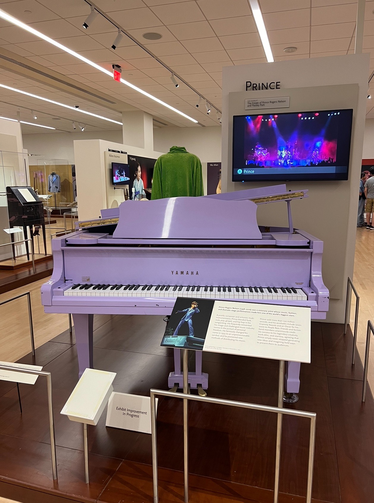 alt txt = "Lavendar piano and green stage costume from Prince at the MIM museum."