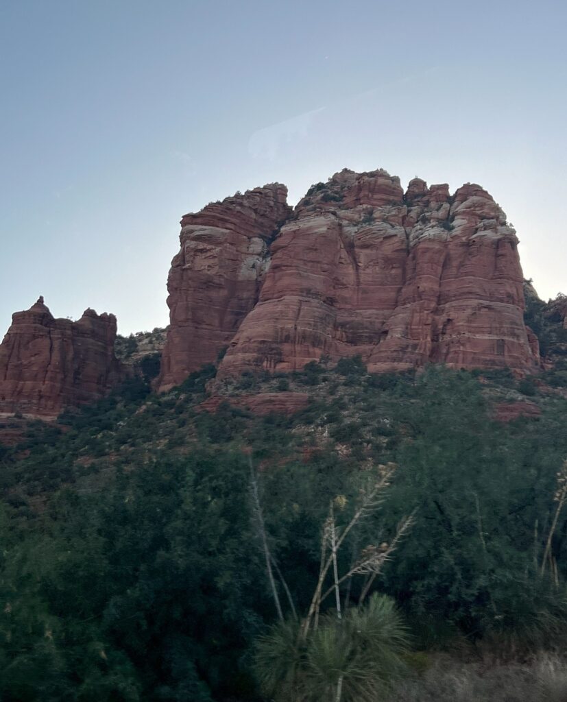 alt = "Red rock mountain formations. surrounded by green vegetation."