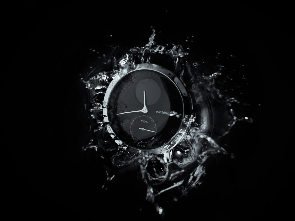 alt txt = "Black and silver watch surrounded by water splash."