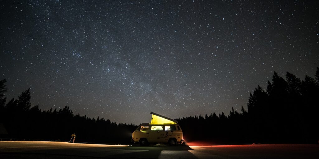 alt txt = Yellow camper road trip van underneath a starry night sky".