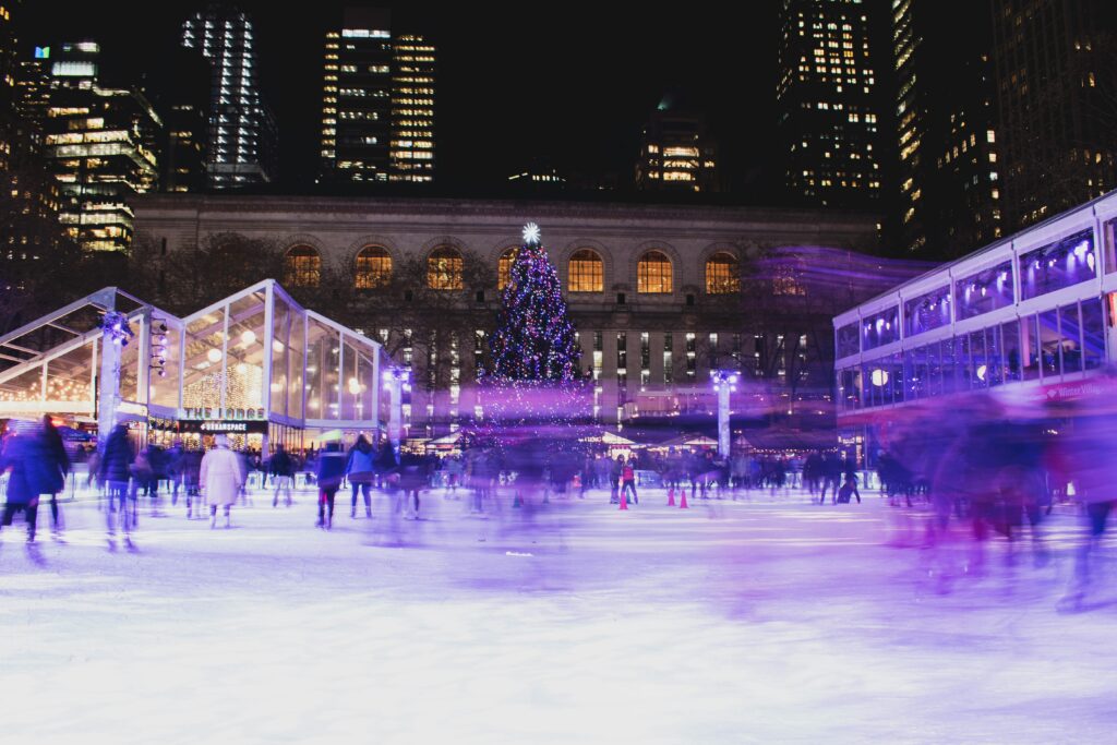 alt txt = "People ice skating at night surrounded by white igloos and tall buildings at Bryant Park".