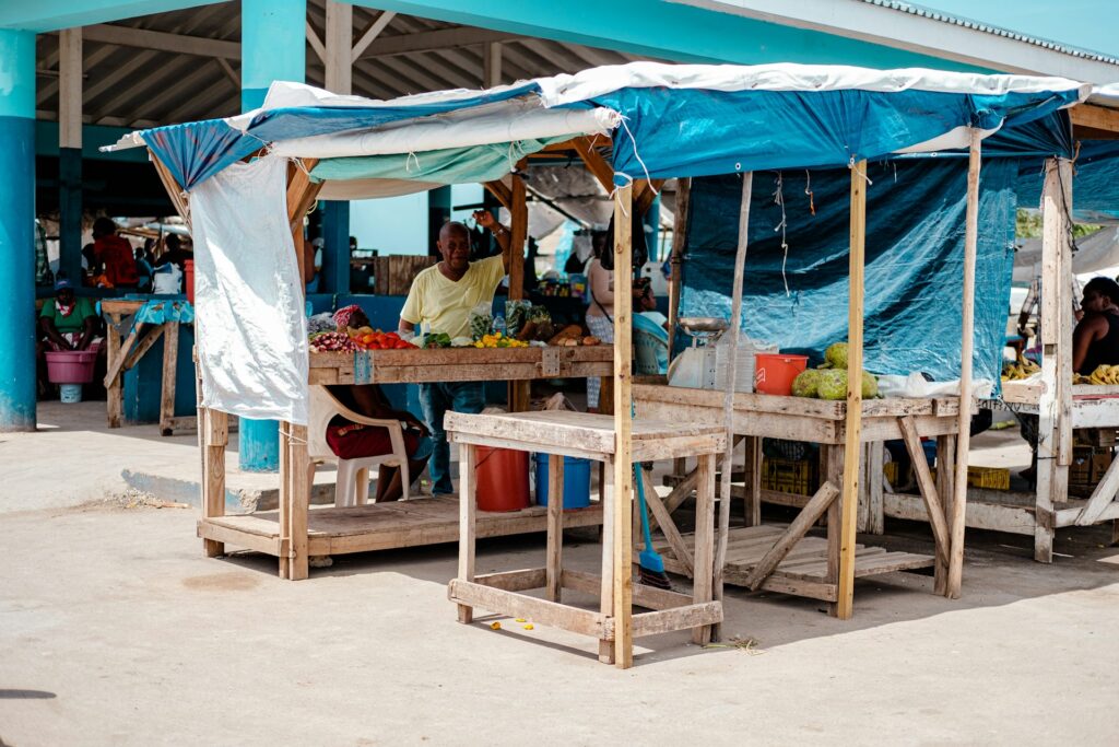 alt txt = "Local market surrounded by fruits and vegetables being sold by residents".