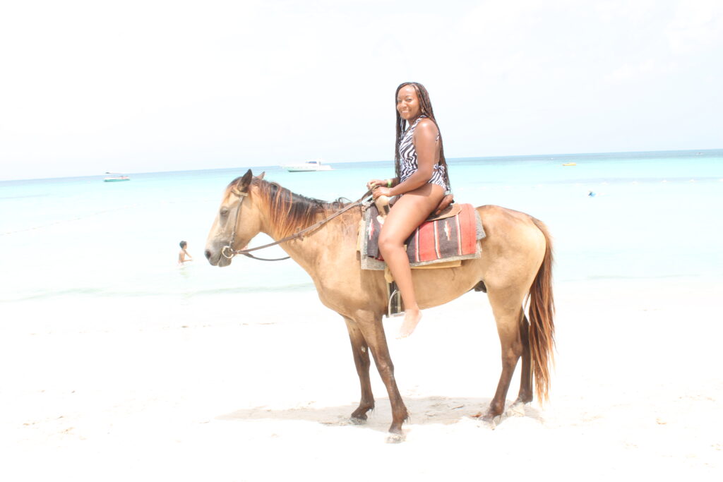 alt txt = "African American woman horseback riding on the beach surrounded by clear blue water in Negril Jamaica".