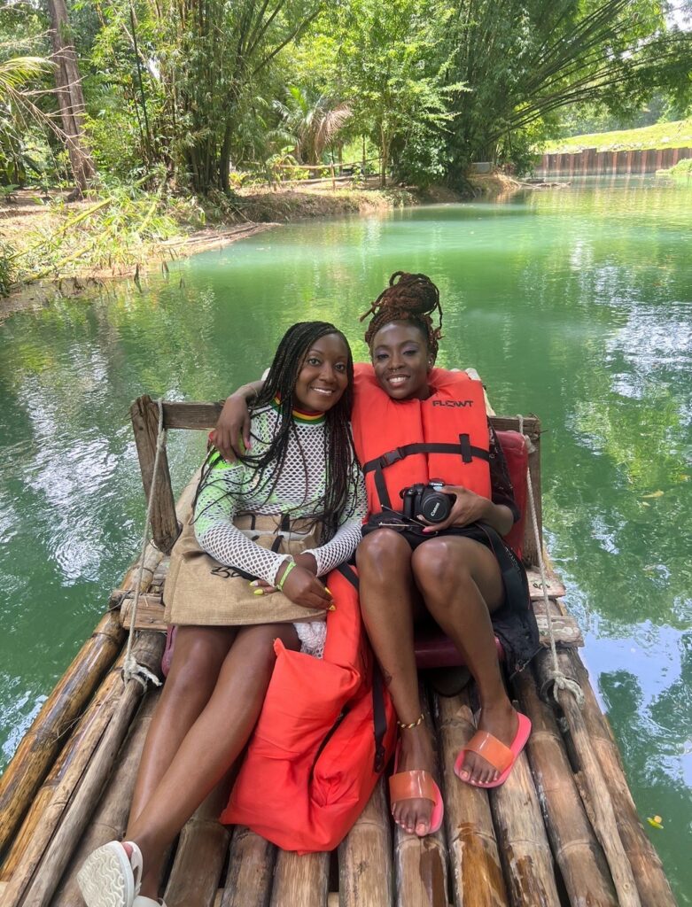 alt txt = "Two African American women on a bamboo raft floating down the Martha Brae river".