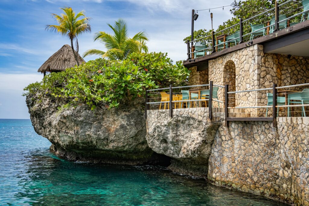 alt txt = "House on a cliff above water surrounded by lush greenery".