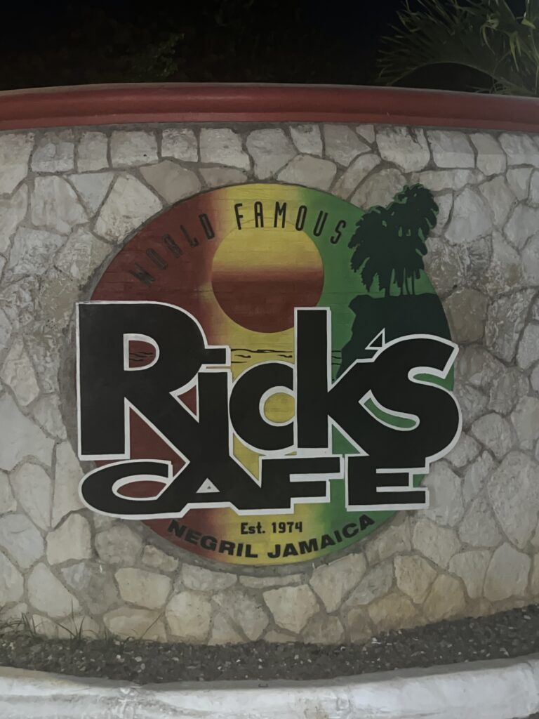 alt txt = " Caribbean restaurant sign in green, red and yellow for Rick's Cafe".