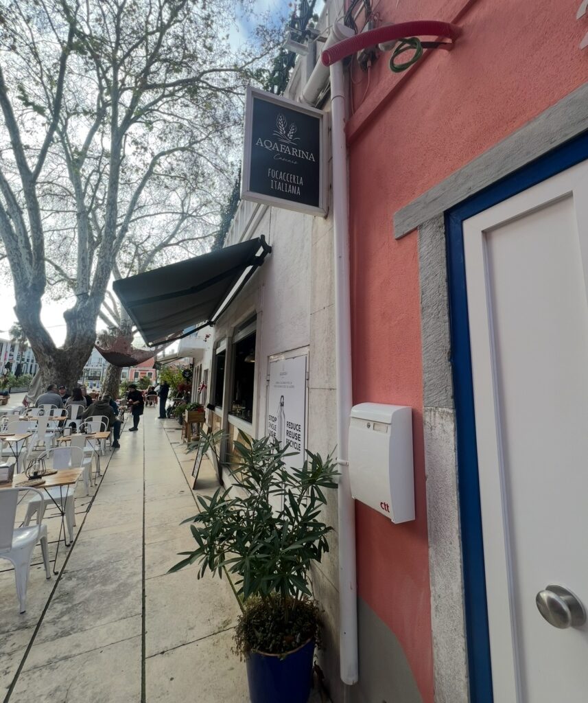 alt txt = "Blue and white sign on a pink building with people walking by".