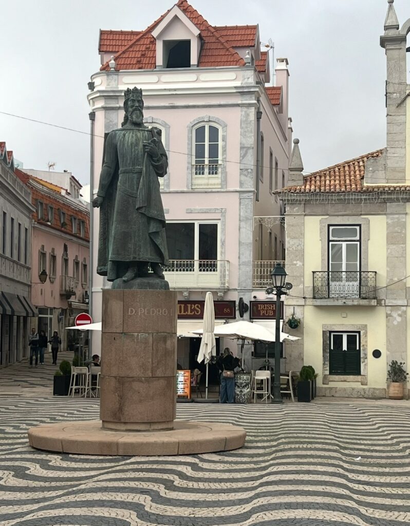 alt txt = "Green statue atop stone in middle of town square".