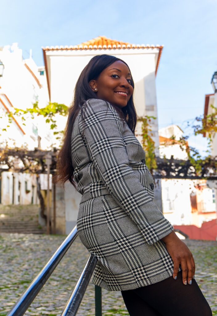 alt txt = "African American woman with long black hair wearing a grey black and white striped two piece outfit and black tights".