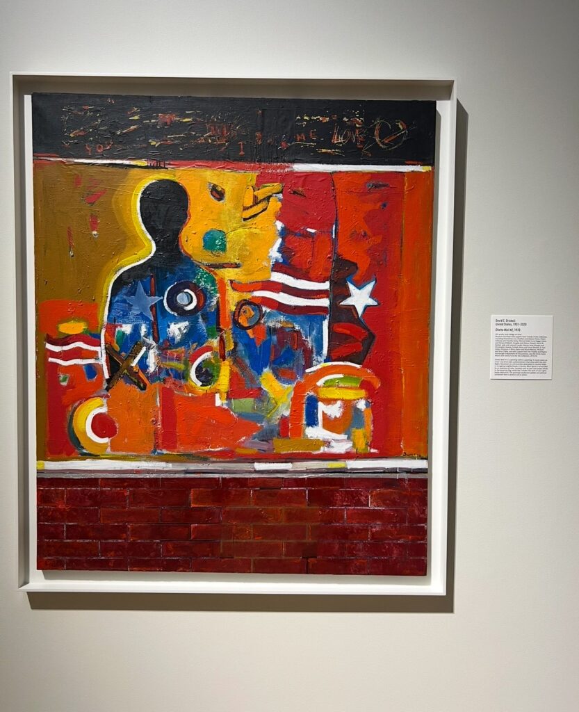 Vibrant mixed-media painting depicting a silhouette of a human figure surrounded by abstract shapes, stars, and American flag-like elements in bold red, yellow, orange, and blue tones. The bottom of the piece is textured to resemble a brick wall, and there are faint inscriptions and layered brushstrokes throughout the artwork.