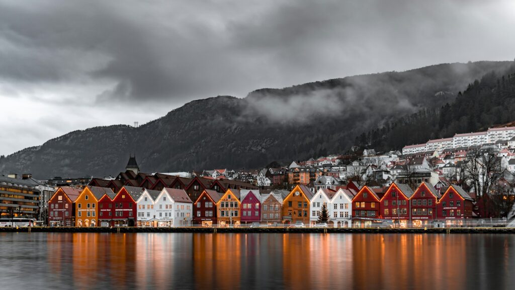 Bergen, NorwayColorful wooden buildings line the waterfront in Bryggen, Bergen, Norway, with mountains and mist in the background on a cloudy day.