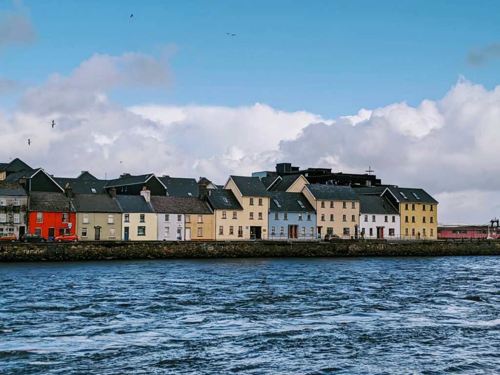 Galway, IrelandRow of colorful waterfront houses known as the Long Walk in Galway, Ireland, with cloudy skies and choppy sea in the foreground.