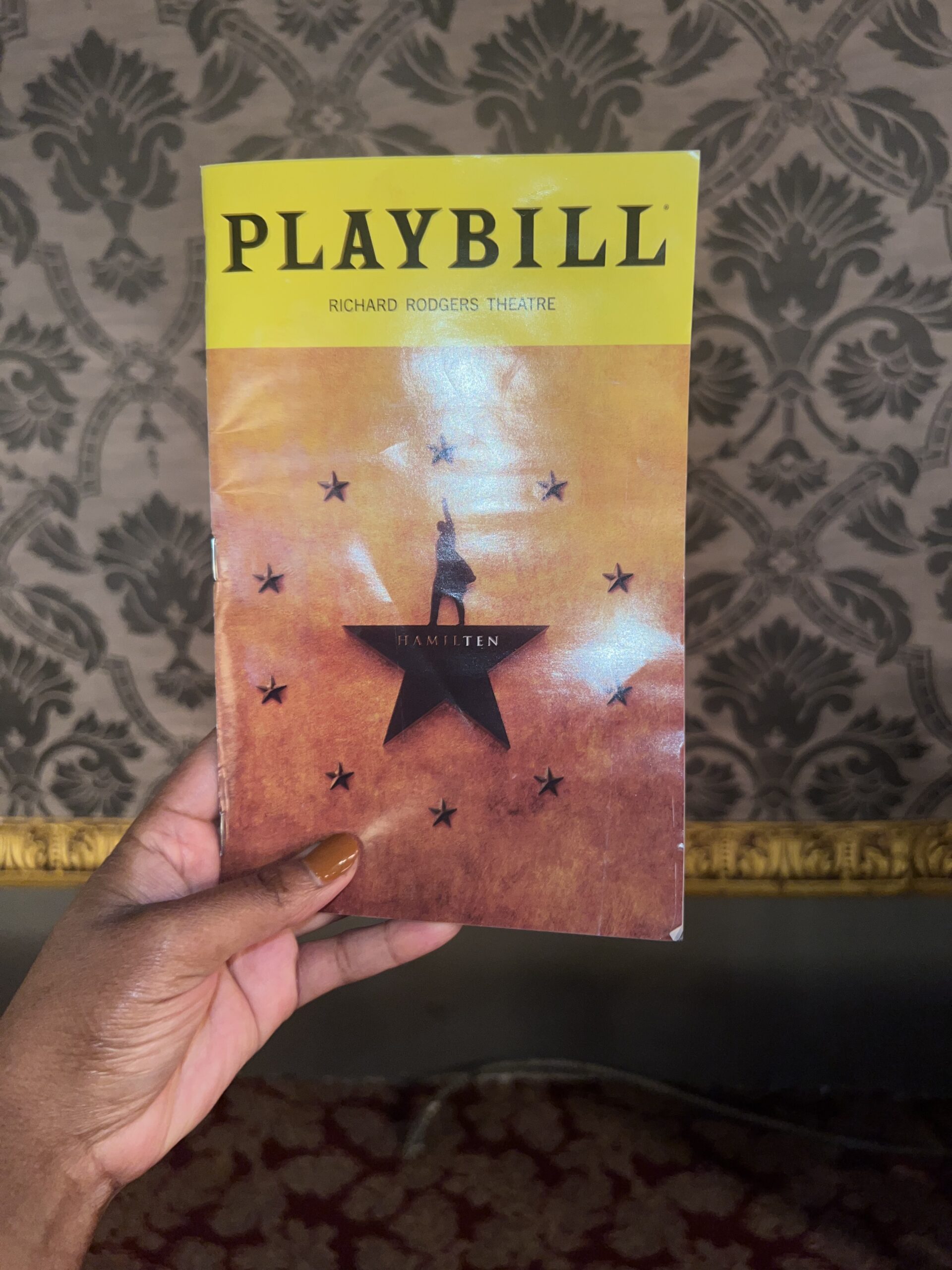 Hand holding a Playbill for Hamilton at the Richard Rodgers Theatre, featuring the iconic logo with a silhouette against a gold background. 