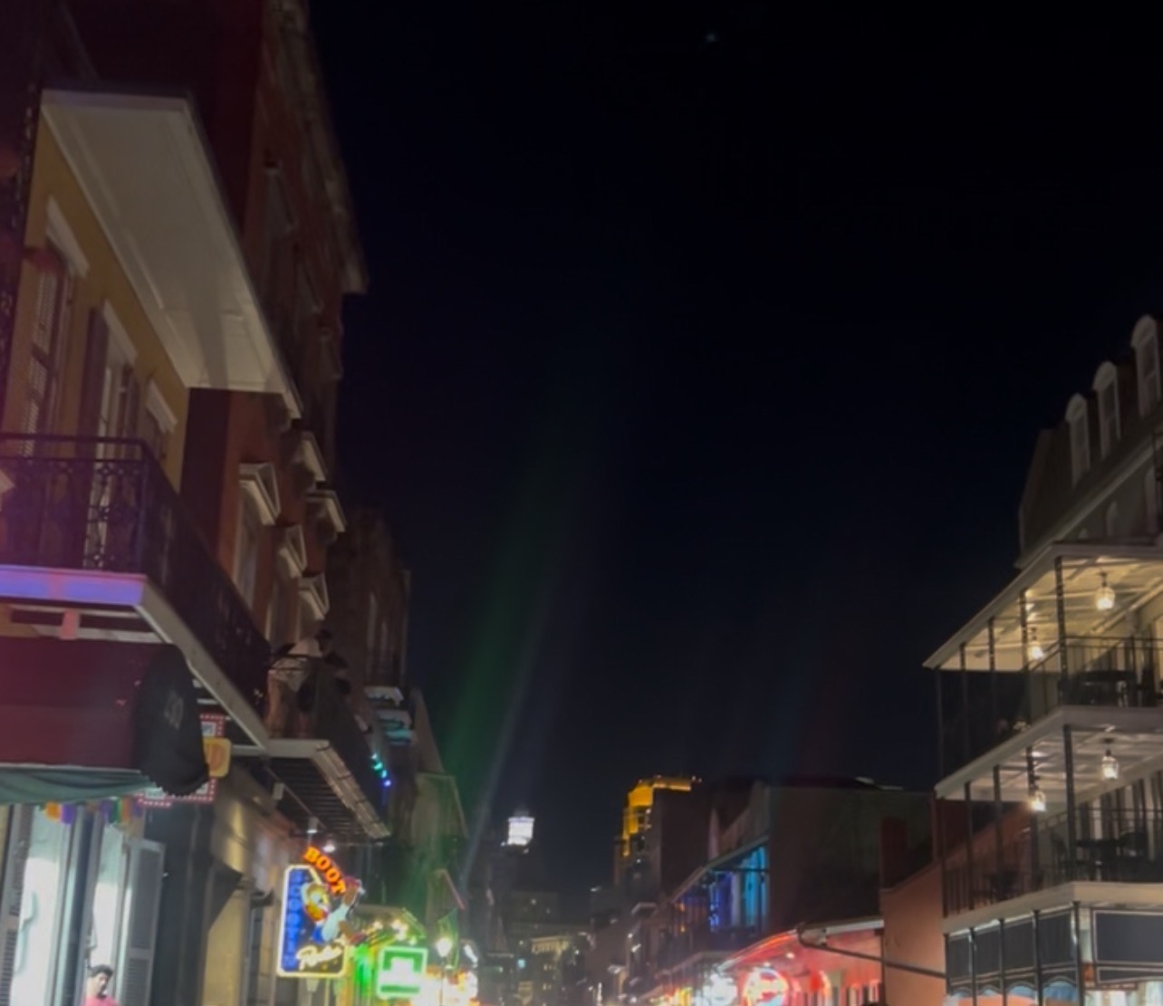 Night view looking down a lively street lined with balconies, neon signs and glowing lights.