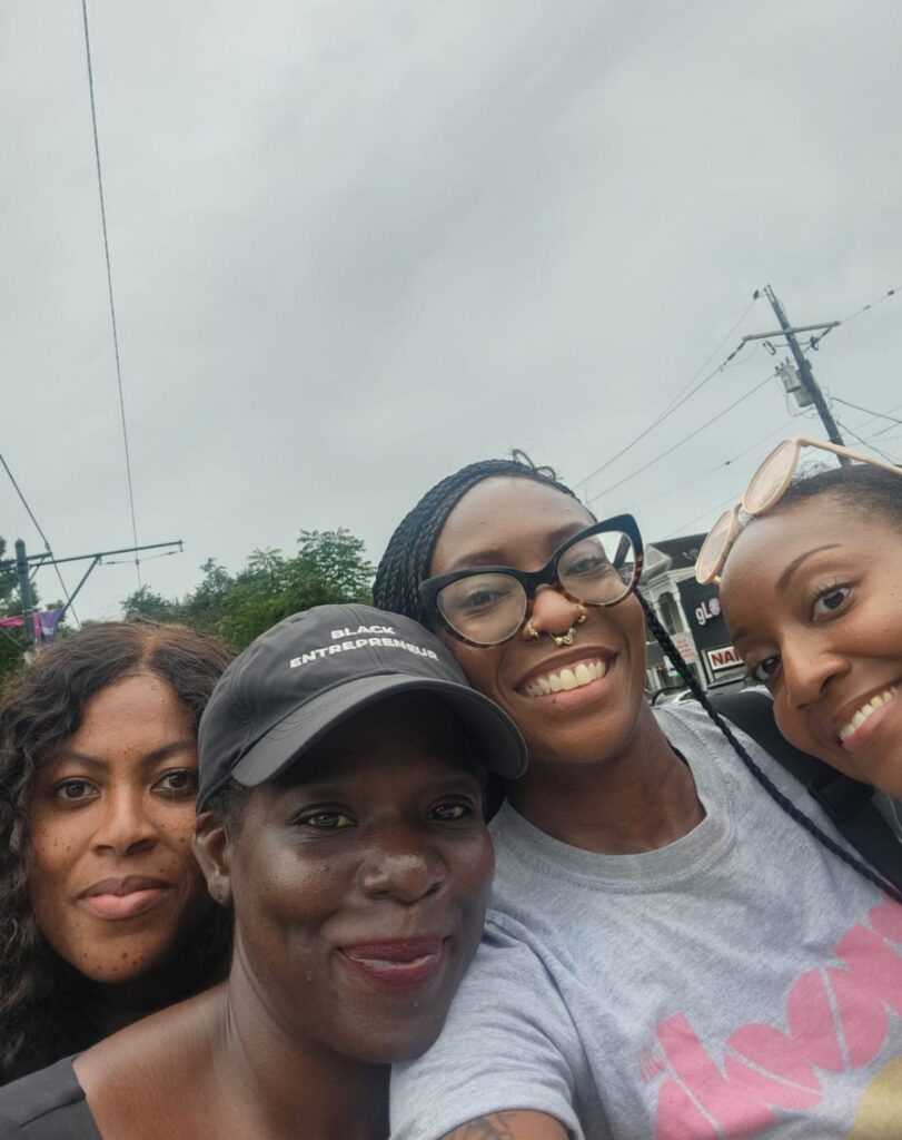 Four women smiling in New Orleans and posing closely for a selfie outdoors, with power lines and buildings visible in the background on an overcast day.