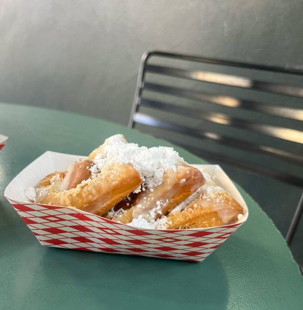 A tray of golden fried dough pieces topped with pralines, powdered sugar and drizzled icing on a green table at Loretta's.