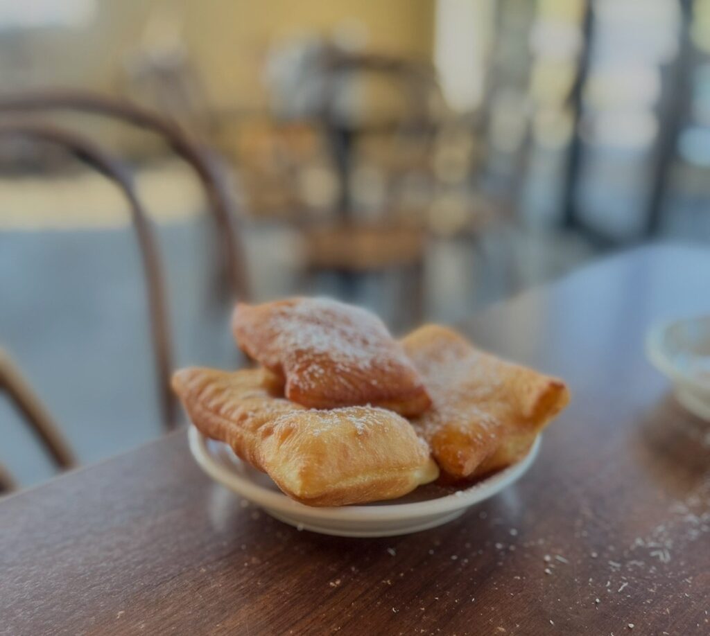A small plate of golden beignets dusted with powdered sugar on a café table. 