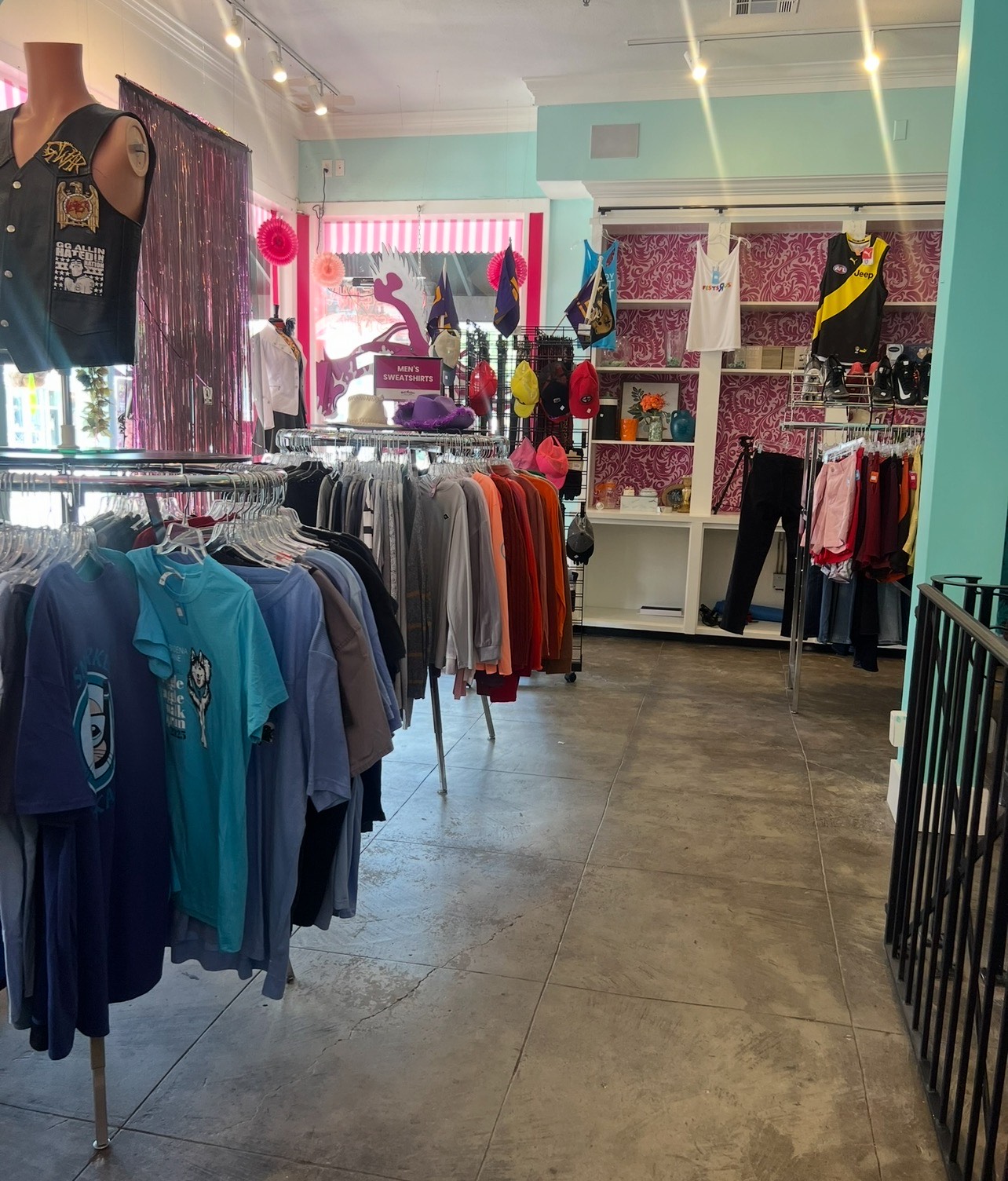 Interior of a thrift store with clothing racks, graphic tees, and colorful décor on display. 