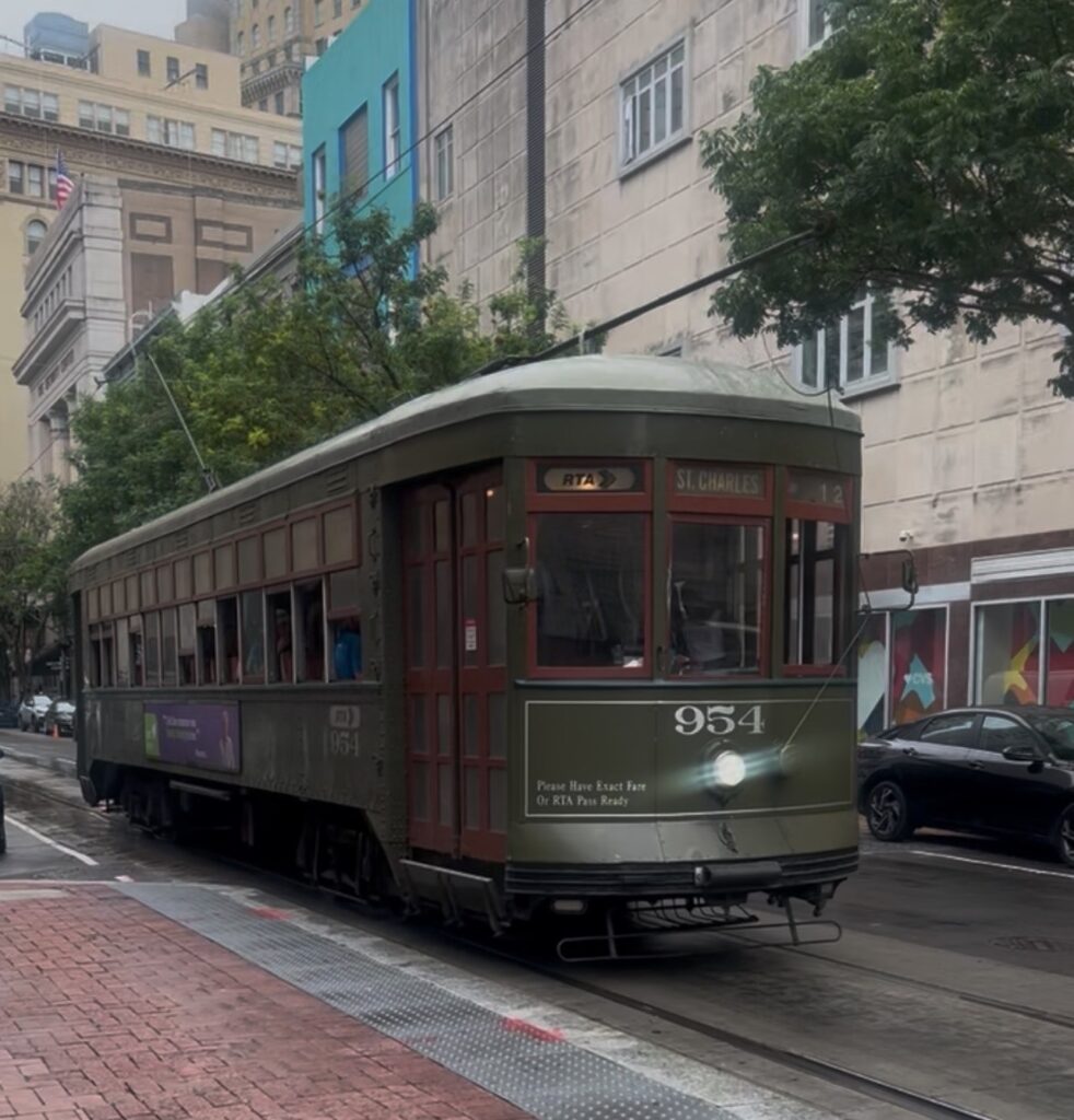 A historic green New Orleans streetcar traveling down a city street lined with buildings and trees.